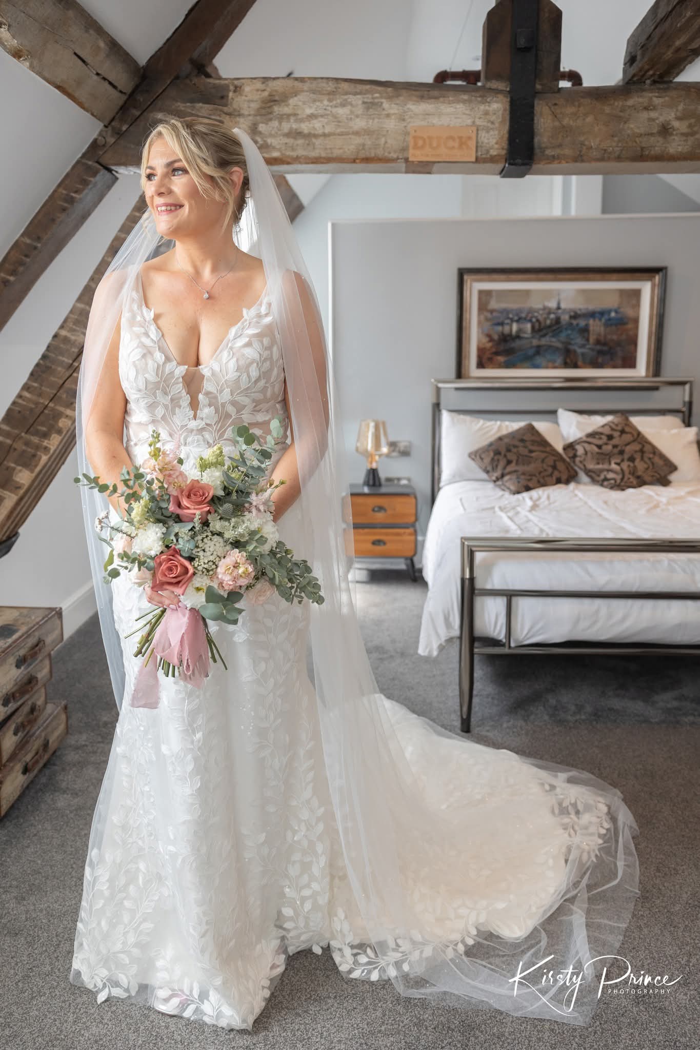 Bride in a white wedding dress holding her white and pink bridal bouquet in a bedroom setting.