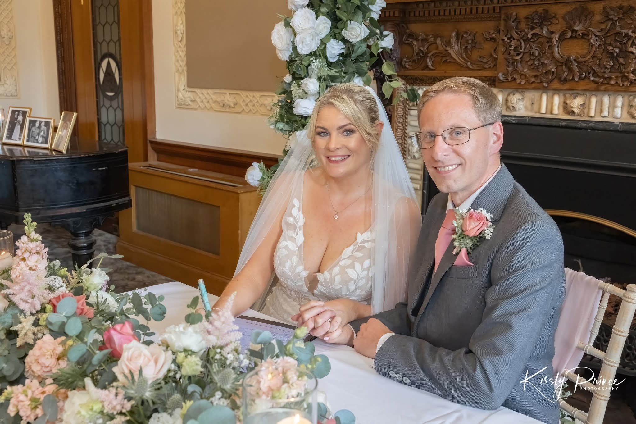 Couple (Helen & Chris) sitting at a decorated table with floral arrangements, smiling for the camera.
