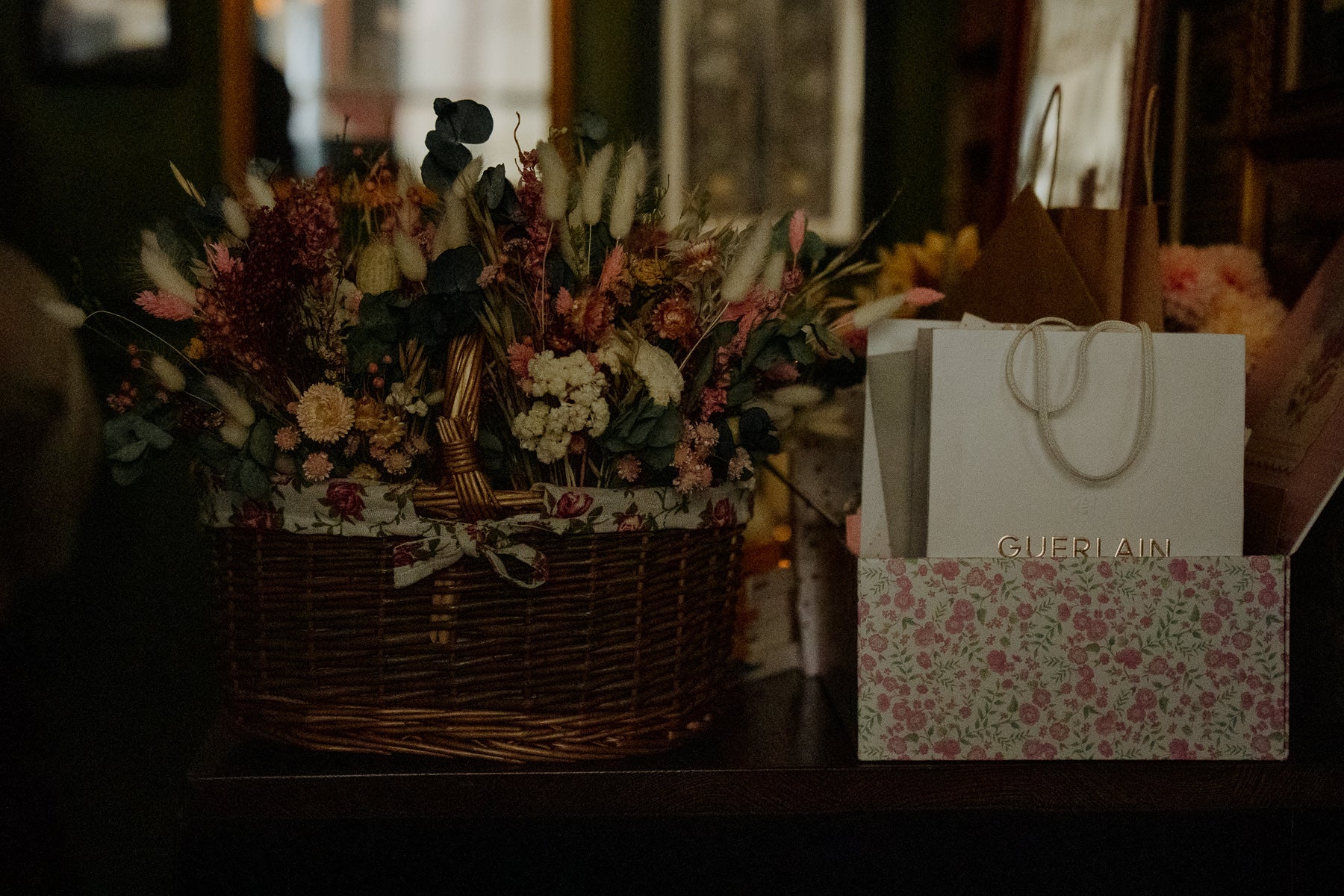 Dried floral arrangements in a basket next to a Guerlain gift bag on a dark surface