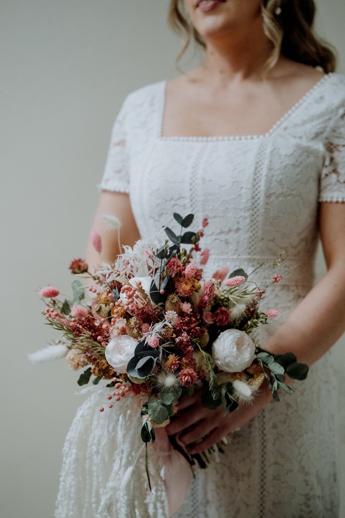 Bride holding a pink and green dried flower bouquet. 