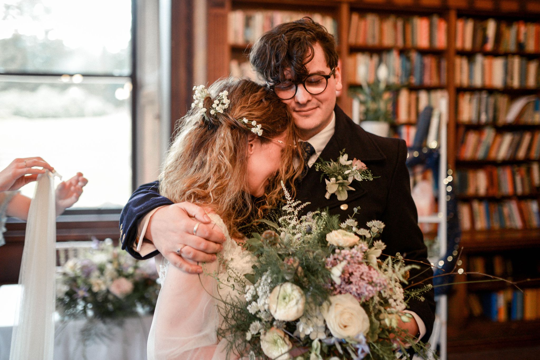 Couple (Rhi & Louis) in a library holding each other with floral bouquets