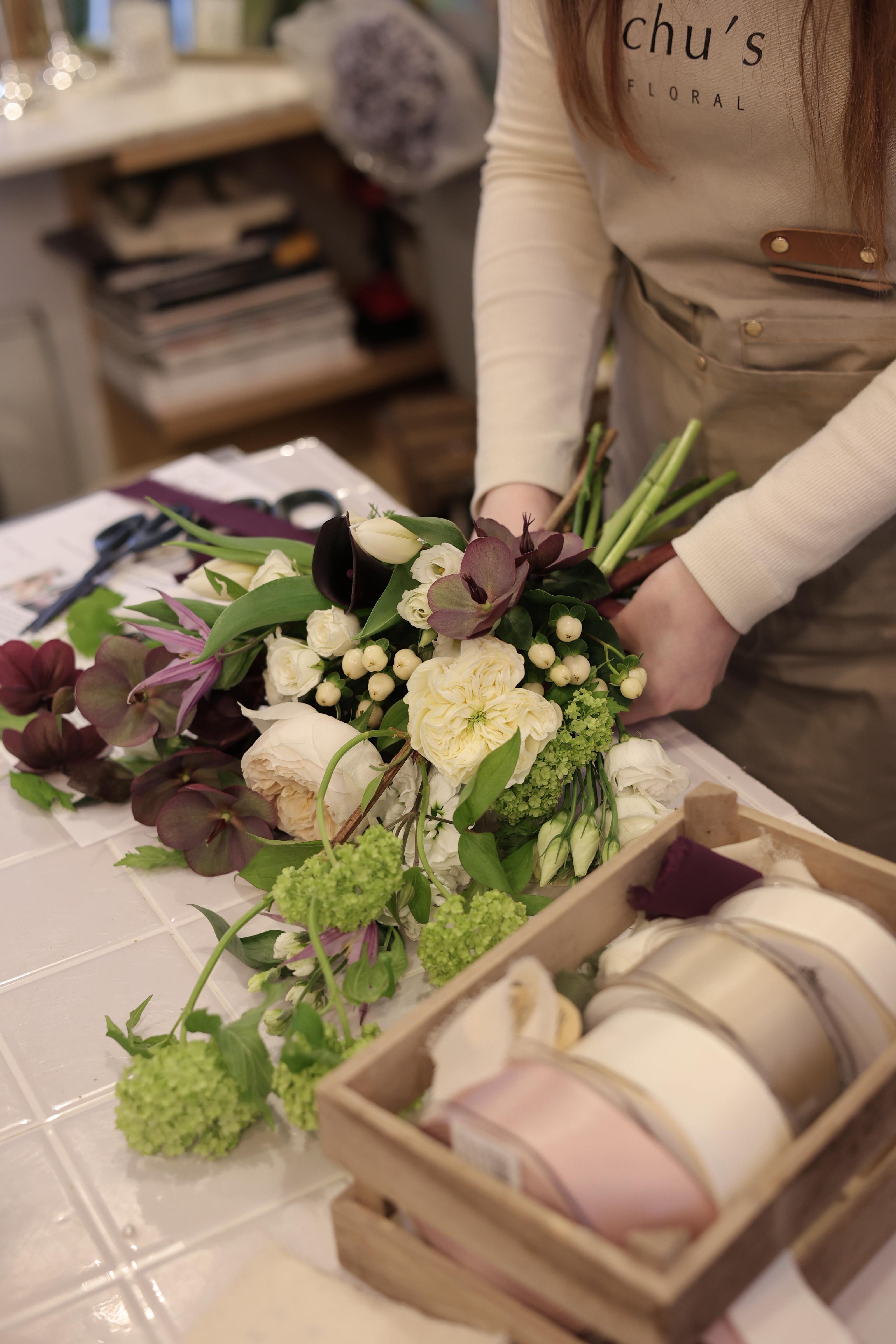 Jordan (Blooming Edens owner) arranging  a bridal bouquet with a box of ribbons on a table.