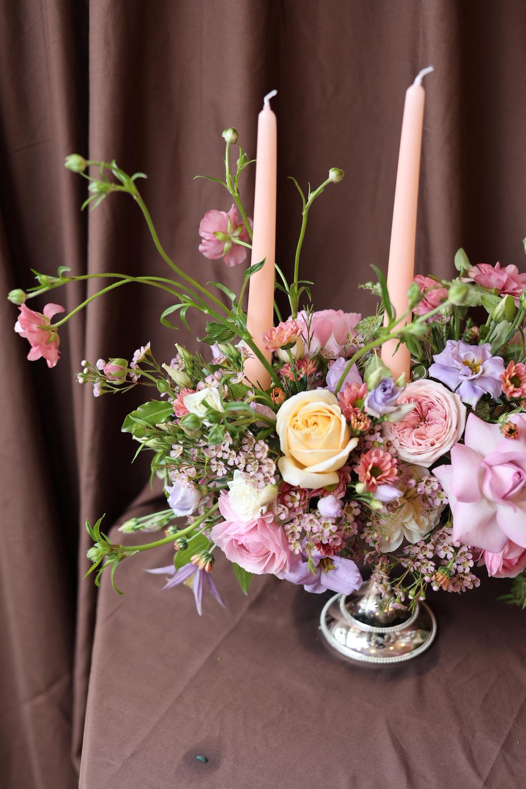 Floral candelabra arrangement with candles on a brown background